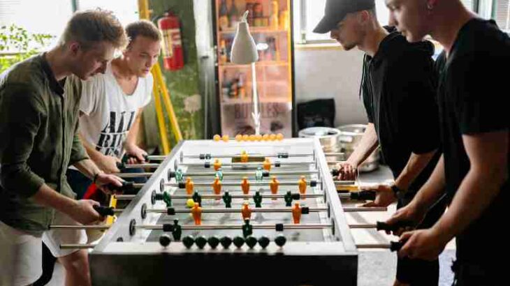 Four young men intensely playing foosball in a lively indoor space., tags: und - pexel